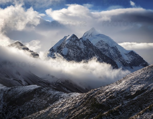 A stunning view of a snowy mountain peak rising above the clouds, with a blue sky background.
