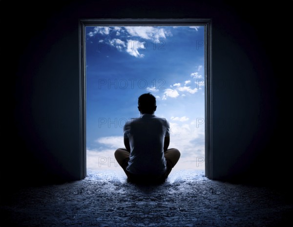 Silhouette of a person sitting alone within a brick archway, observing a peaceful and scenic cloudy