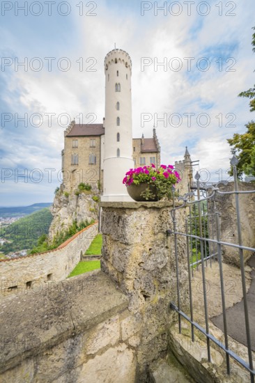A tall tower with pink flowers in a stone wall arrangement in front of a castle, Lichtenstein