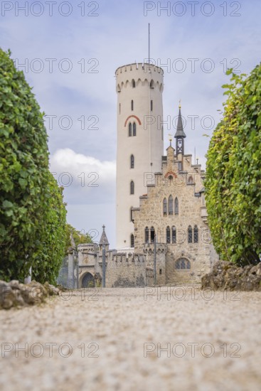 Majestic castle with towers and manicured hedges, captured from a view along a cobbled path,