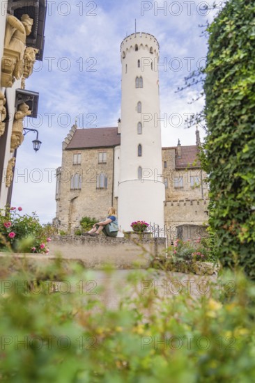 Woman sitting quietly in a castle garden in front of a high tower, Lichtenstein Castle,
