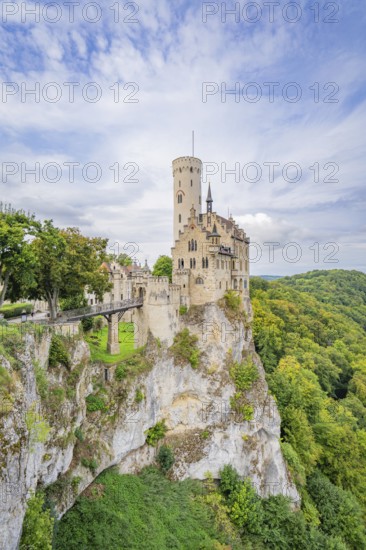 Medieval castle with high tower on a rocky outcrop surrounded by lush green forests and dramatic