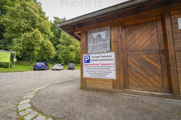 A small car park with a wooden hut and parked cars at the edge of the forest, Lichtenstein Castle,