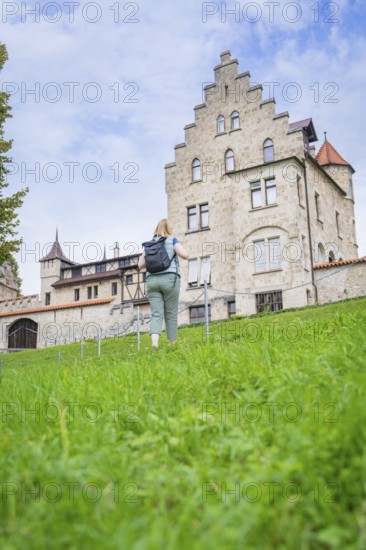 A woman walks up a grassy hill towards an imposing historic castle, Lichtenstein Castle,