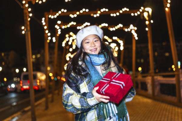 Smiling young woman holding christmas present enjoying winter holidays season under decorative