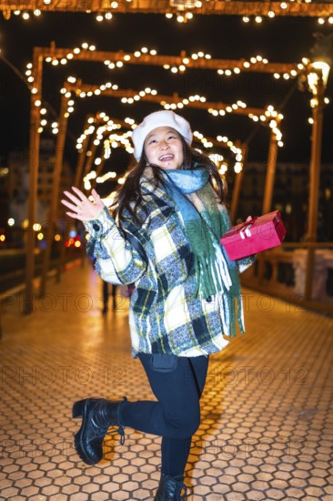 Happy young woman holding a christmas gift, reveling in the enchanting glow of festive lights and