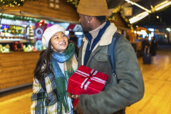 Young multiethnic couple joyfully holding a beautifully wrapped christmas gift while enjoying the
