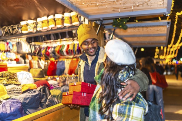 Happy multiethnic couple exchanging christmas presents at a stall in a christmas market at night