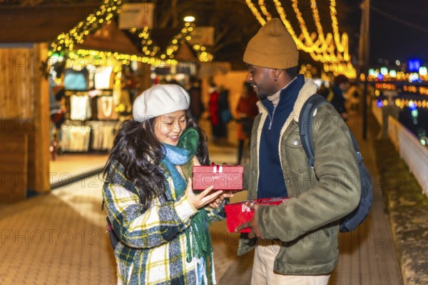 Happy multiethnic couple exchanging christmas gifts at a festively decorated christmas market,