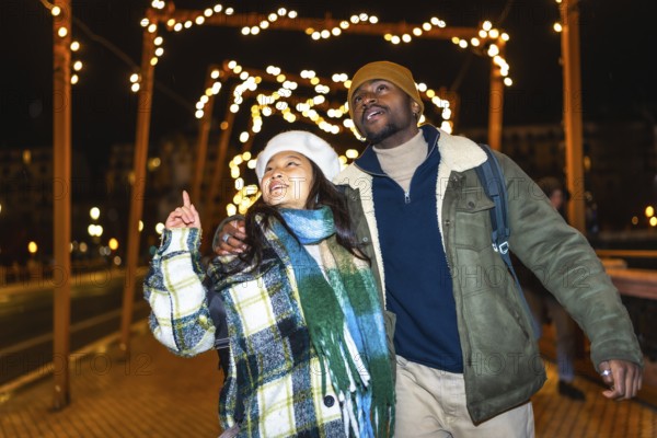 Young multiethnic couple walking hand in hand, admiring the enchanting christmas lights and festive