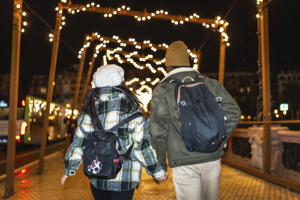 Multiethnic couple walking on bridge at night, holding hands and enjoying christmas lights
