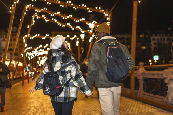 Young multiethnic couple walking on bridge with christmas lights, enjoying winter holidays