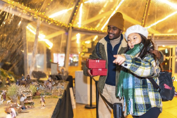 Happy multiethnic couple holding christmas gifts and admiring a nativity scene at a christmas