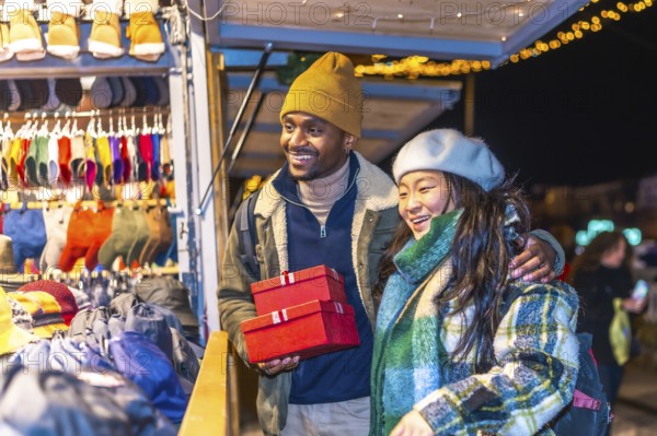 Multiethnic couple enjoying christmas shopping at a decorated christmas market, holding red gift
