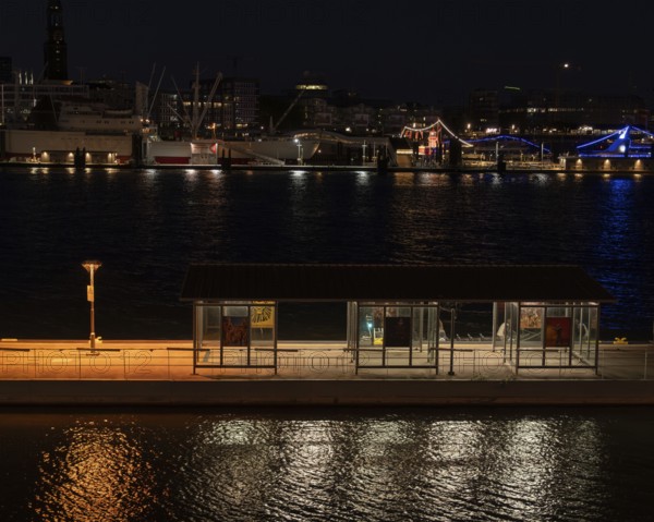Night shot of a pontoon with bus shelter at the theatre on the Elbe with a view of the lighting of