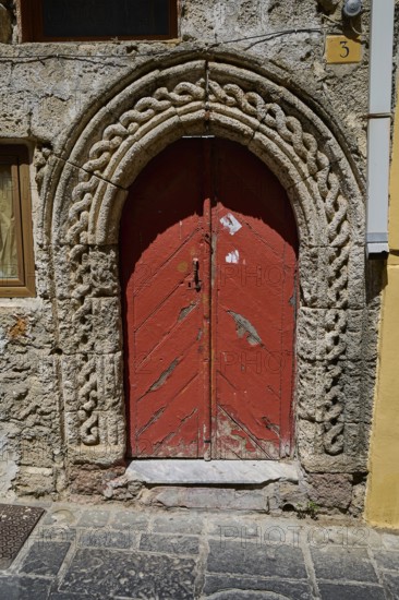 Red door with Romanesque arch and decorative stone carvings in an old façade, Turkish Quarter,