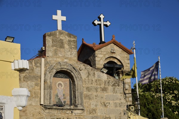 Church of Agios Panteleimon, stone church with crosses and flags in the background under a blue