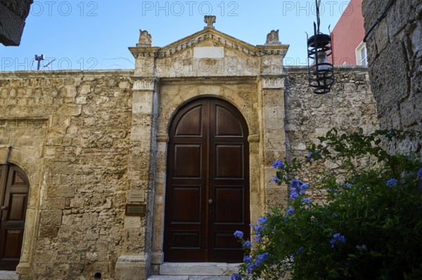 Gate of a synagogue, Massive wooden door in an old stone wall under a blue sky with blooming