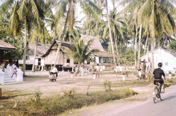 Traditional village houses in coconut palm trees, boys and young men playing Sepak Takraw foot
