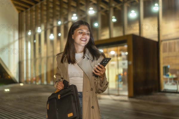 Young businesswoman smiling while checking her smartphone, holding a briefcase and walking alone on