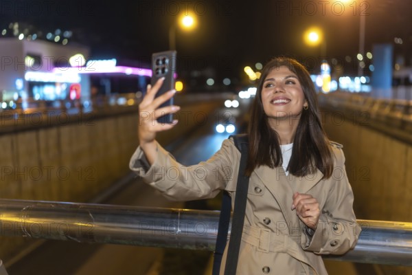 Young woman smiling and holding a smartphone, capturing a selfie against the bright, blurred lights