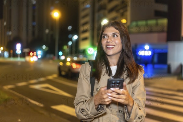 Young woman smiling and looking away while using a mobile phone on a pedestrian crossing, waiting