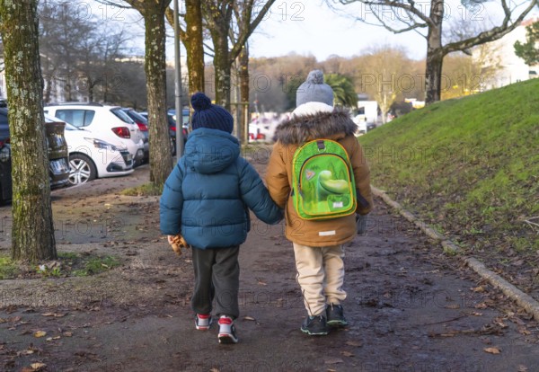 Two young children holding hands and walking home from school on a chilly winter day in bayonne,