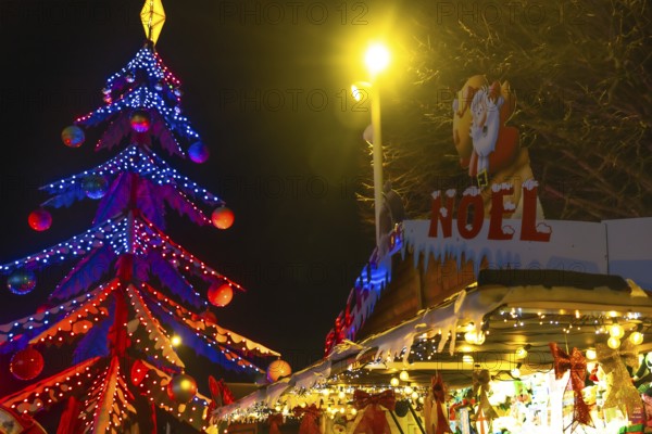 Glowing christmas tree and decorated market stall create festive atmosphere at night in bayonne,