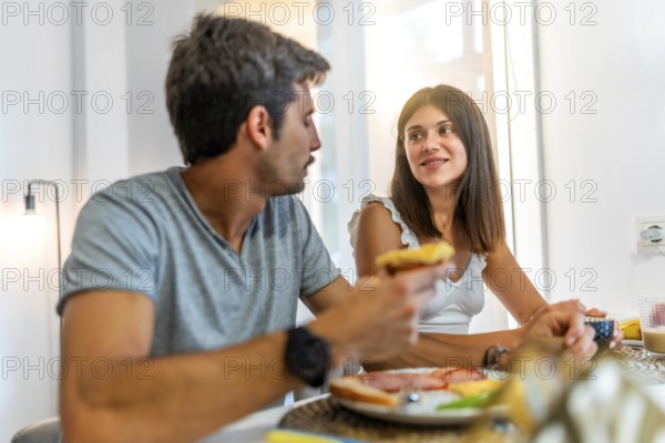 Young couple sharing a meal and conversation at their kitchen table, enjoying a relaxing morning