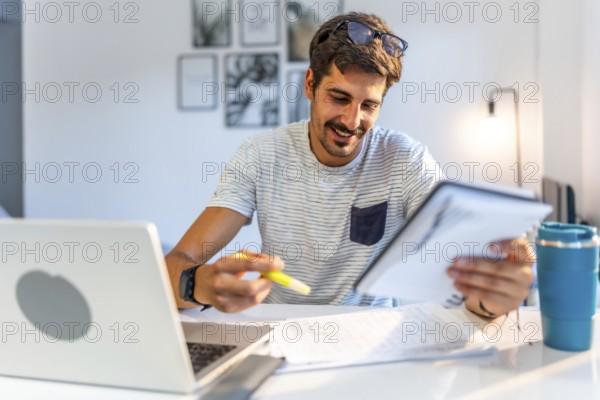Young male freelancer comparing information on his tablet with data on his laptop, working from his