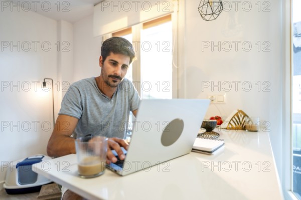 Young man concentrating on his laptop, enjoying a coffee while working remotely from his stylish