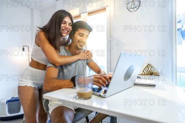 Young smiling couple using laptop at home, woman hugging man working on computer, modern bright