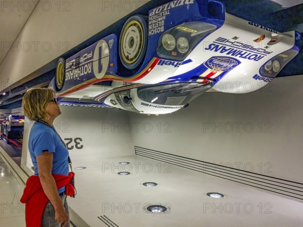 Visitor to the museum looks upwards at a Porsche 956 racing car hanging upside down under the
