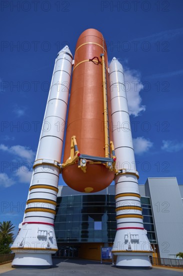 Large orange space shuttle with booster rockets in front of a modern building, Kennedy Space Center