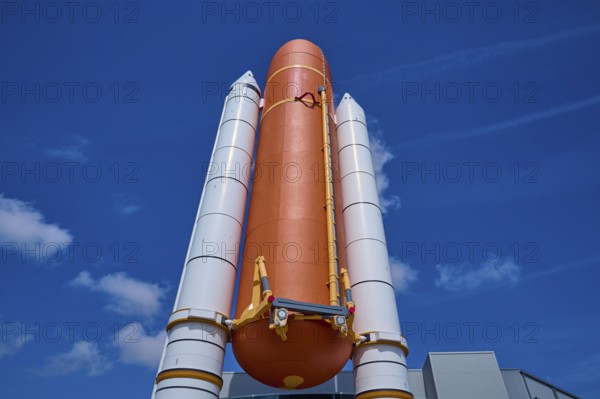 Large orange space shuttle with two launch vehicles against a blue sky, Kennedy Space Center