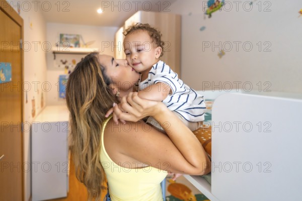 Mom kissing her baby boy in a decorated bedroom, showing love and affection in a cozy home