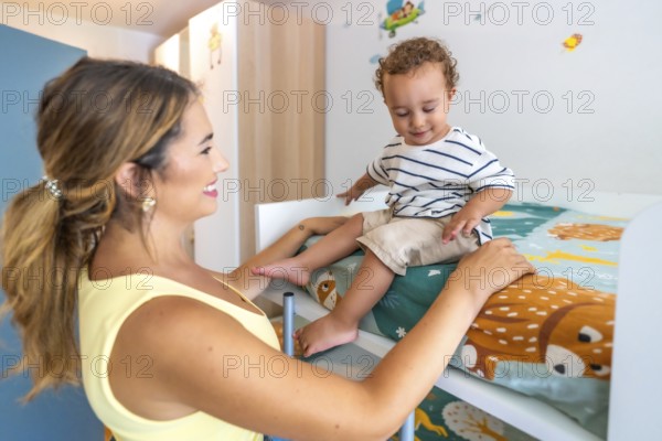 Young mother assisting her little son as he carefully climbs down from a bunk bed in a beautifully