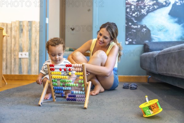 Happy mother watching her baby boy playing with a colorful abacus, developing early math skills in