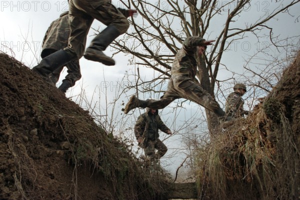 BIH, Bosnia, Brcko, 07.01.1996, Bosnian and American soldiers jump over a former trench