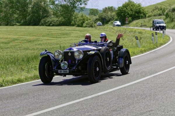 Black classic car with waving driver on winding road in idyllic landscape, classic car, car race,