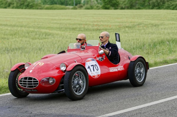 A classic red car with two people driving on a country road, classic car, car race, Mille Miglia,