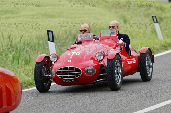 A red sports car with two drivers drives on a rural route, classic car, car race, Mille Miglia,