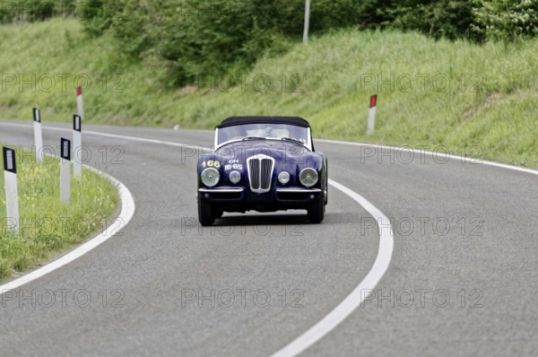 A dark classic car drives alone on a winding country road, classic car, car race, Mille Miglia,