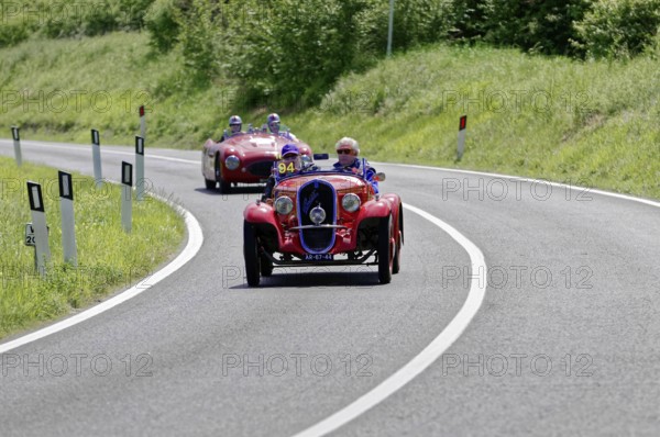 Red classic car in a sharp bend, followed by other classic cars on a country road, classic car, car