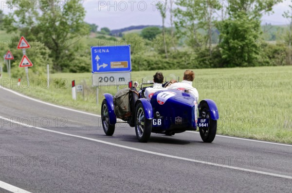 Blue classic car in the direction of Siena on a country road through the Italian countryside,