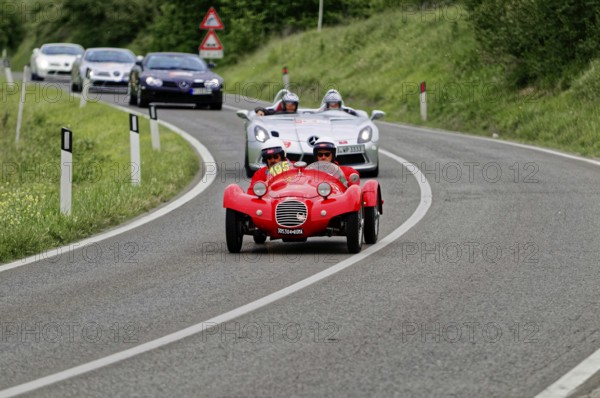 Two people with helmets in a red classic car on a country road, sporty-classic scene, classic car,