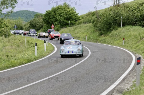 Blue vintage car leads a group of classic cars on a winding country road, picturesque surroundings,
