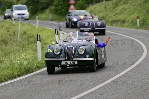 Two people in a green vintage convertible on a winding country road, casual atmosphere, vintage