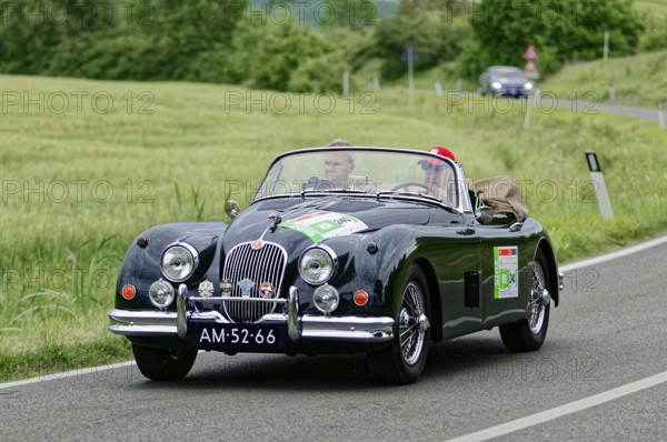 Black convertible driving on a country road through an idyllic landscape, classic car, car race,