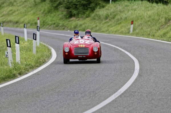 A red convertible sports car with two drivers on a winding country road, classic car, car racing,